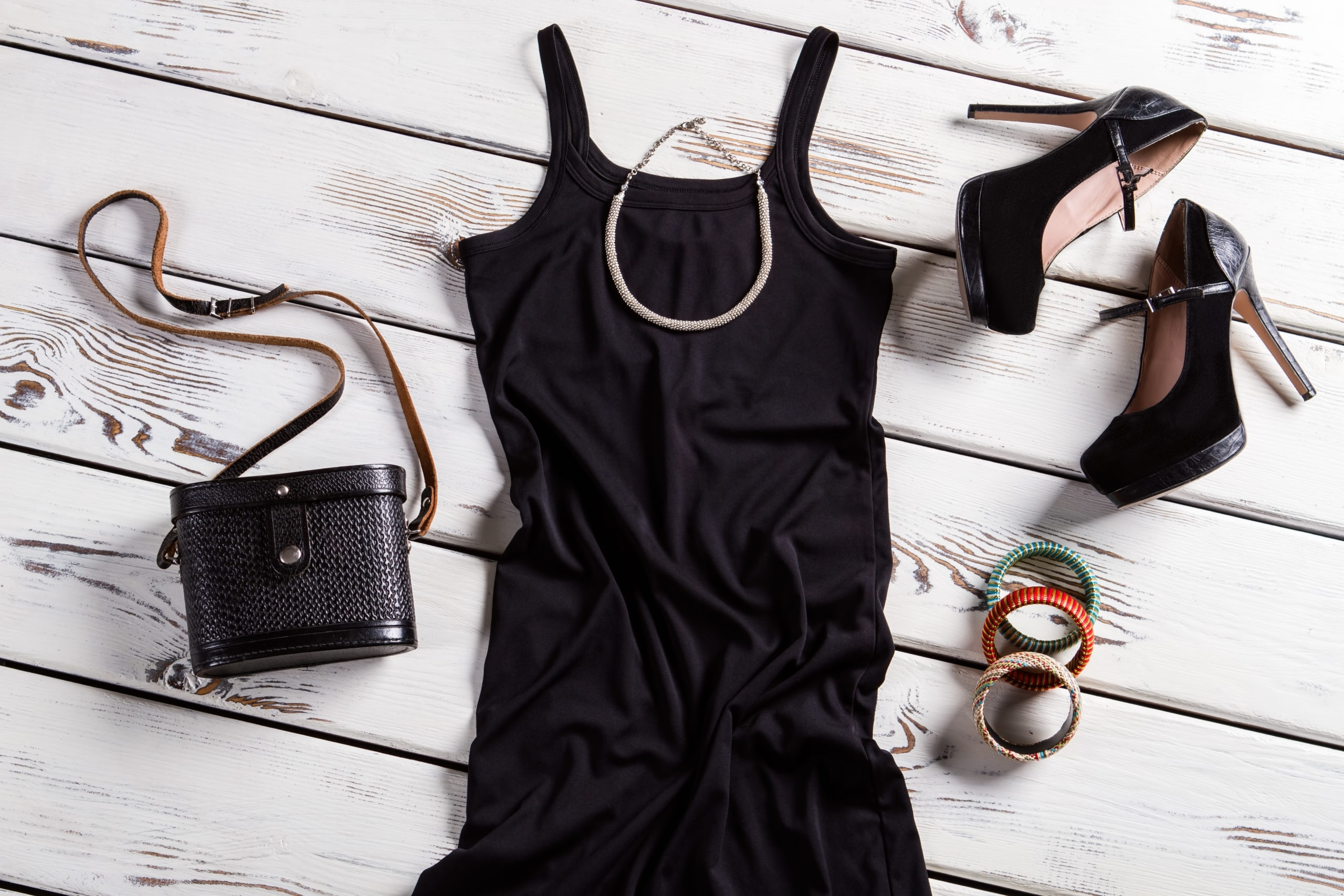 Black dress and small necklace. Jewelry and clothes on shelf. Frosted heel shoes and accessories. Suede shoes and retro purse.